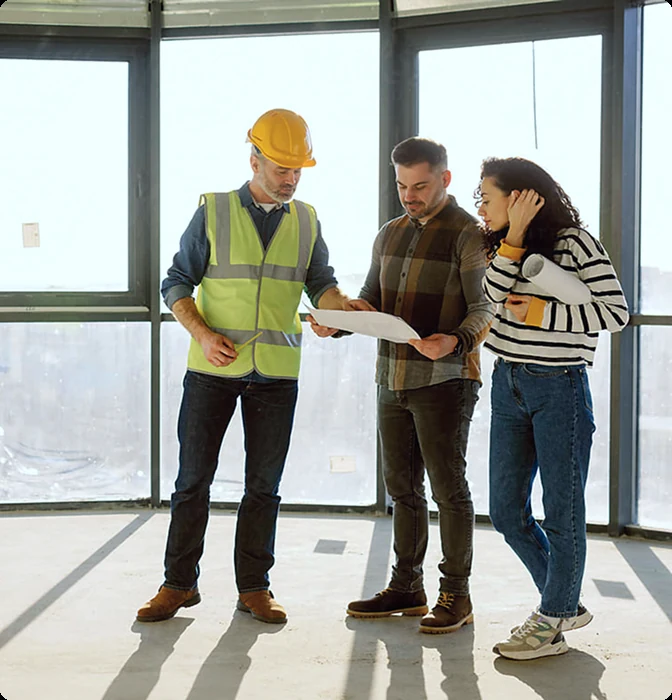 Ein Bauleiter und zwei Kunden besprechen Baupläne auf einer Baustelle