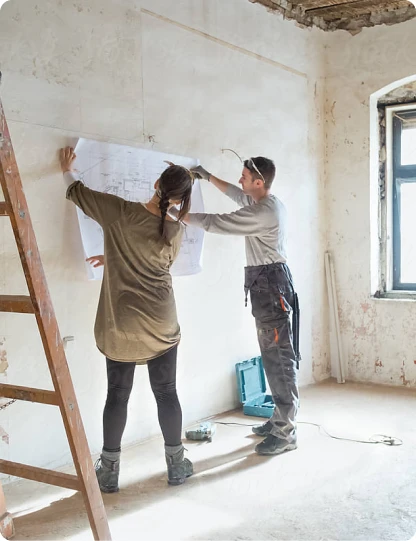 Zwei Handwerker markieren Baupläne an einer unverputzten Wand