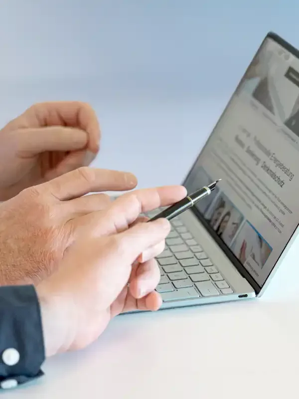 Eine Hand hält einen Stift über ein aufgeklapptes Notebook mit einer Übersicht