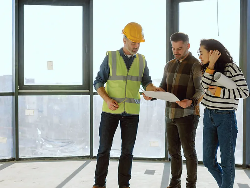 Bauleiter mit Helm und Warnweste bespricht Baupläne mit Kunden auf einer Baustelle