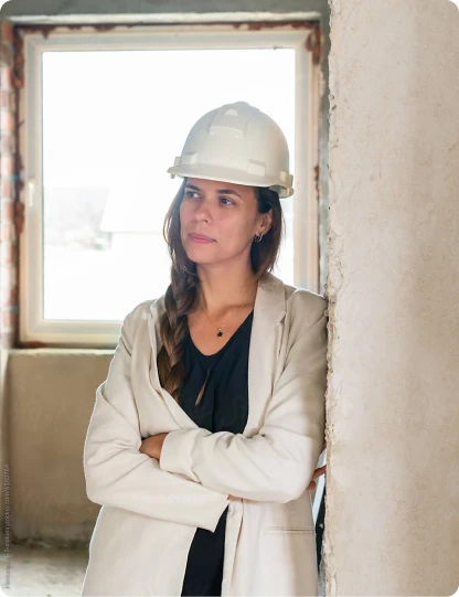 Eine Frau mit Bauhelm steht nachdenklich auf einer Baustelle