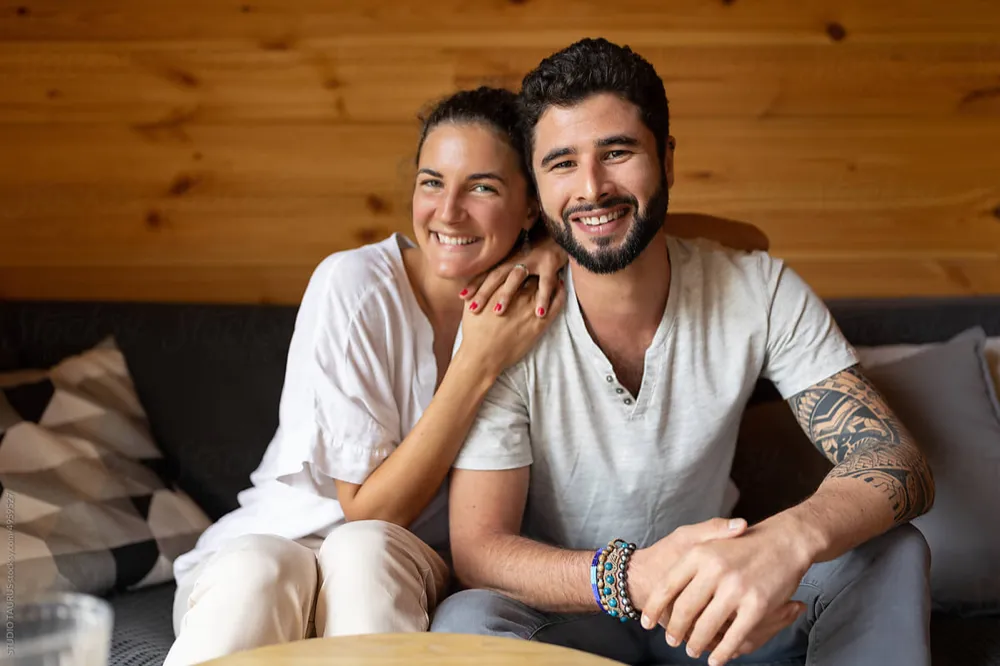 Sandra L. und Alexander K. lächeln gemeinsam auf dem Sofa