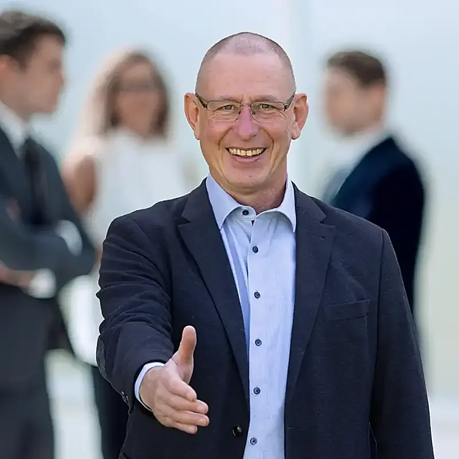 Energieberater lächelt und streckt die Hand zur Begrüßung aus, im Hintergrund unterhält sich sein Team